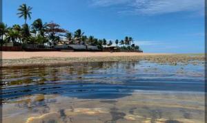a beach with palm trees and a house in the distance at Casa espaçosa em Itacimirim com piscina e churrasqueira! in Camaçari