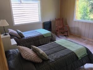 a bedroom with two beds and a chair and a window at Cabaña con costa de arroyo in San Martín de los Andes