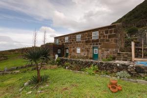 a stone building on a hill with a palm tree in front at Caldeira Guesthouse in Fajã da Caldeira de Santo Cristo