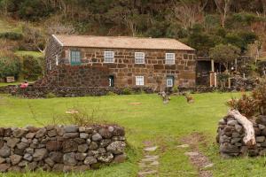a stone house with a stone wall in front of it at Caldeira Guesthouse in Fajã da Caldeira de Santo Cristo