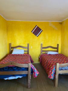 two beds in a room with a yellow wall at Qocha Simi Homestay in Ocosuyo