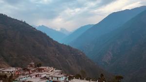 a village on a mountain with mountains in the background at Chaukhamba Pine Cottage & HomeStay in Rānsi