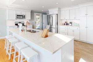 a white kitchen with a large white island with stools at Island Bay Bungalow in Eastham