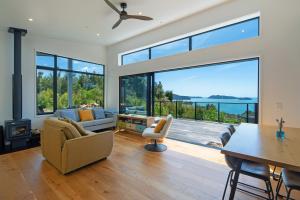 a living room with a table and chairs and large windows at Kokomea in Kaiteriteri