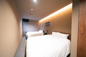 two beds in a room with white sheets at Mon Hotel HAKATA in Fukuoka