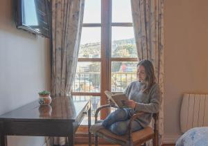 Hotel Boutique Casa Vander في فالبارايسو: امرأة تجلس على كرسي تقرأ كتاباً أمام نافذة