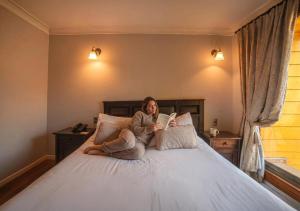 Hotel Boutique Casa Vander في فالبارايسو: امرأة تجلس على سرير تقرأ كتاباً