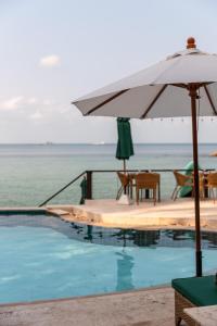 a swimming pool with an umbrella and the ocean at Beyond The Blue Horizon Boutique Bungalows in Haad Chao Phao