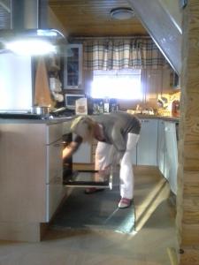 a woman bending over to look into an oven in a kitchen at Kuulapää Chalet in Äkäslompolo