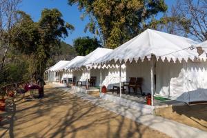 a row of white tents with tables and chairs at Omya Forest Camps & Cottages Bir, Near Choti Machiyal in Bīr