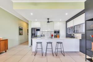 a kitchen with white cabinets and bar stools at The Skyline Lookout Pool, BBQ, FREE parking in Stuart Park