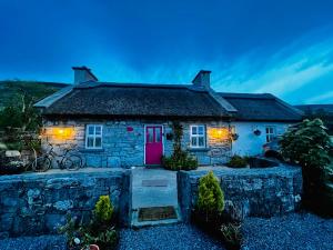 a stone house with a pink door and lights at Oranuisce Thatch Cottage Ballyvaughan in Ballyvaughan