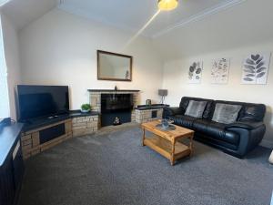 a living room with a black leather couch and a tv at Dun-Niall Apartment in Oban