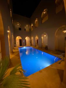 a large swimming pool in a building with a blue pool at Riad Dar Fatima in Merzouga