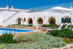 a white building with a pool and an umbrella at Masseria Gorgognolo in Ostuni
