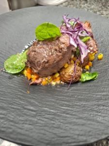 a piece of meat on a black plate with vegetables at Gîte chez Maritxu in Saint-Étienne-de-Baïgorry