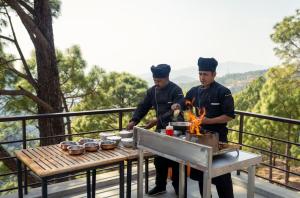 two men are cooking food on a table on a balcony at BluSalzz Escapade Resort Lansdowne in Lansdowne