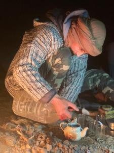 a person sitting on a table with a tea pot at Desert mountains camping in Merzouga