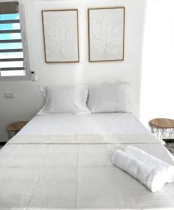 a white bed in a white bedroom with two pictures on the wall at Studio Colibri vue mer in Quartier Morne Acajou