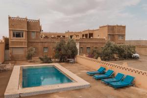an outdoor swimming pool with blue lounge chairs in front of a building at merzouga stars luxury camp in Merzouga