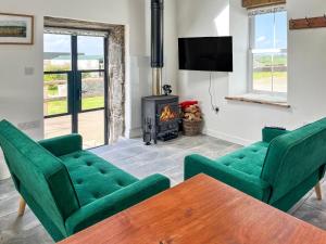 a living room with two green chairs and a stove at Landberrick Farm Bothy 2 in Newton Stewart