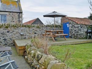 a picnic table with an umbrella next to a stone wall at Haven Cottage - E4342 in Holy Island +2 photos