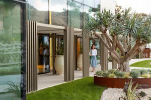 a woman walks past a building with a tree in front at Legacy Ithos Boutique Hotel in Porto Santo