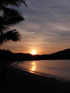 a sunset on a beach with a palm tree at Emil's Beach Cottage in El Nido