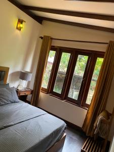 a bedroom with a bed and windows and a desk at Farm House Villa in Ratnapura
