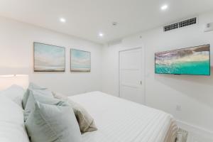 a white bedroom with a bed and three paintings on the wall at Villa Verde - Boca Pool & Beach Walk in Boca Raton