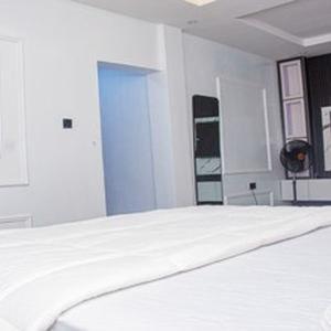 a white bedroom with a bed and a blue door at Tomfrank Hotel in Ado