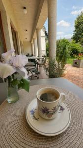 a cup of coffee on a table with a vase of flowers at Éden Panzio in Bük