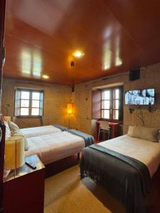 a bedroom with two beds and a table and two windows at Pousada Torre Lombarda in Allariz