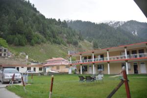 a building with chairs in a field next to a mountain at Pine Hills, Naran in Naran