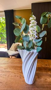 a white vase with a plant in it on a table at Panterhuis Leo l Tiny House l Buitenbad, airco, speeltuin, bostuin in Epe +17 photos