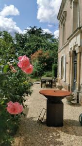 a bird bath in front of a building with pink roses at Fleurs et Abeilles in Faye-lʼAbbesse