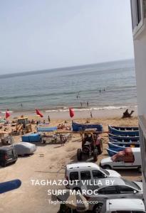 a beach with chairs and people on the water at Sharing is caring Taghazout in Taghazout