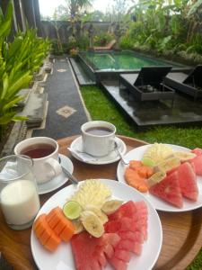 two plates of fruit on a table with cups of coffee at Pulu Sari Suite Ubud in Ubud