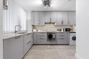 a kitchen with white cabinets and a sink and a dishwasher at Modern 2 Bed Flat 5 mins Ealing Broadway Station in Ealing +2 photos