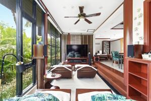 a living room with a ceiling fan and large windows at The Baan Bua Elefant Villa in Rawai Beach