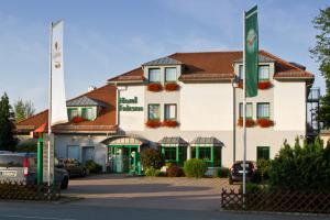 un gran edificio blanco con ventanas verdes en un aparcamiento en Hotel Friesen en Werdau