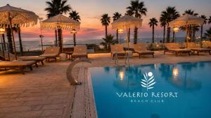 a pool at a resort with chairs and a sunset at Valerio Resort beach club in Margherita di Savoia