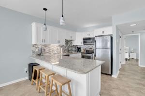 a kitchen with white cabinets and a counter with stools at Corner on Romar 706 in Orange Beach