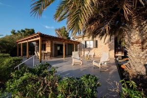 a patio with white chairs and a house at Villa Isabelle on the beach in Paralía Iríon