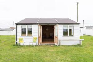 a small white house with two chairs in a field at Bacton Beach Cabin in Bacton +4 photos
