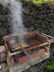 a grill with smoke coming out of it next to a stone wall at Casinha de Pedra in Cais do Pico