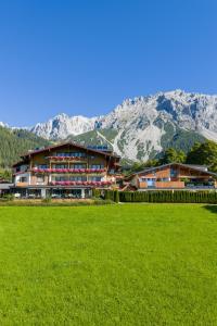 a building with a green field in front of a mountain at Landhaus Ramsau in Ramsau am Dachstein