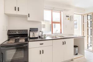 a kitchen with white cabinets and a stove top oven at Sintha Guesthouse in Kraaifontein +7 photos