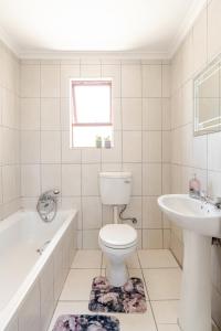 a white bathroom with a toilet and a sink at Sintha Guesthouse in Kraaifontein