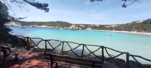 a bench next to a beach with boats in the water at Menorca beach in Cala Galdana +7 photos